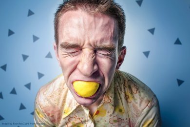 Man biting into a lemon pulling a face