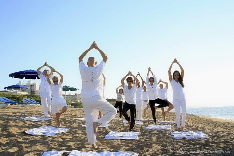 yoga class practicing pose on a beach
