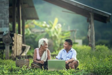 Grandmother and grandson sitting in a garden with a laptop and talking