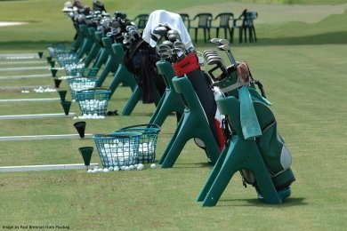 Golf driving range with many golf bags lined up and baskets of golf balls