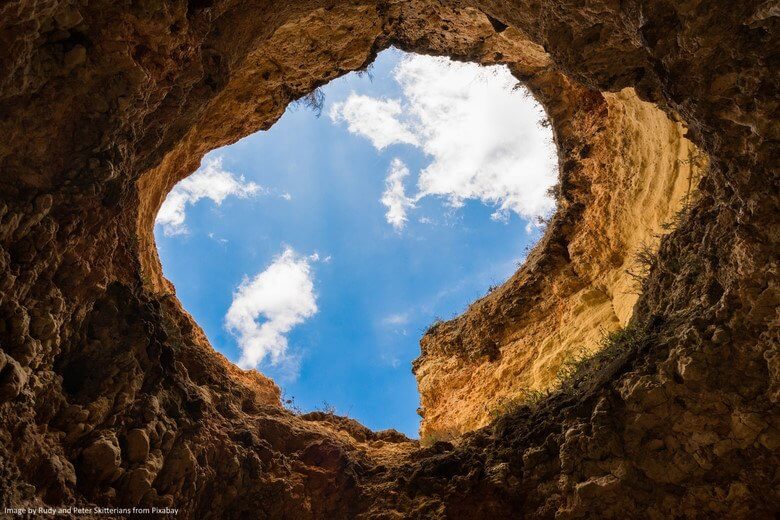 View from a cave or whole in the ground towards a blue sky with white clouds