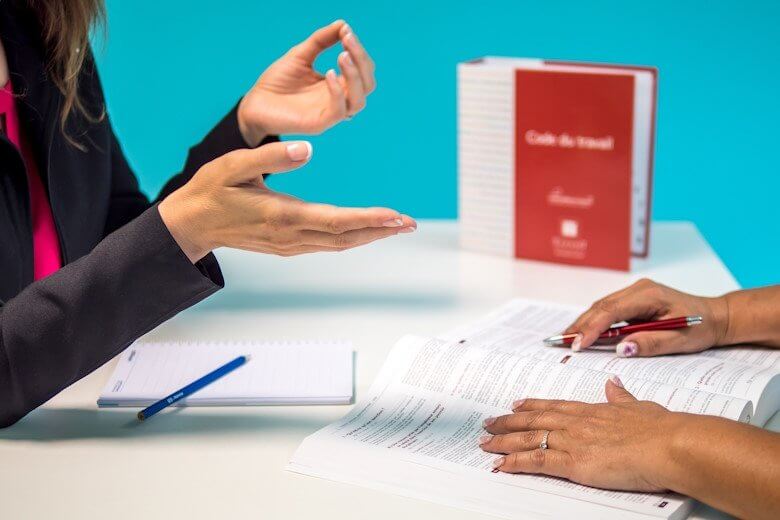 Two office workers sitting opposite on a desk and working through a work book