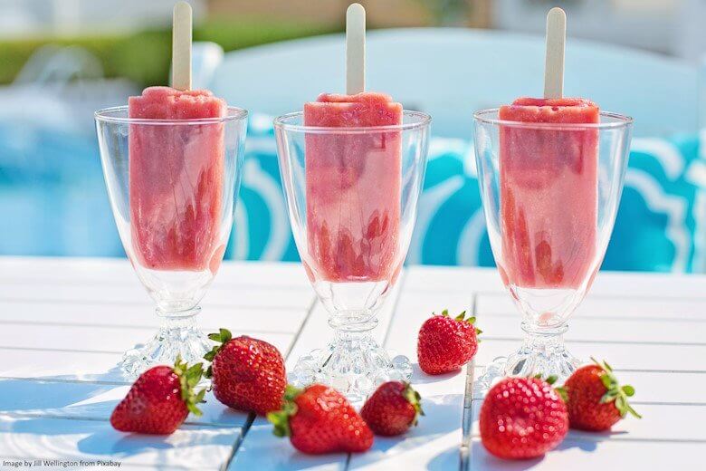 3 glasses with a strawberry ice lolly each and strawberries in front on a table