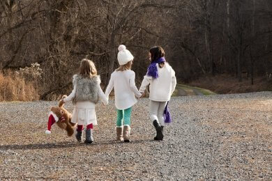 Three children walking outdoors, hand in hand, one carries a teddy with father Christmas hat