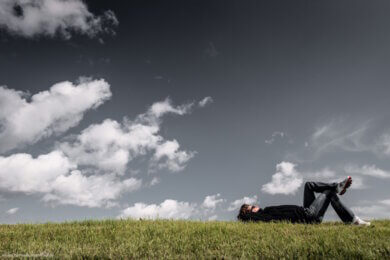 man lying on grass under sky, thinking...