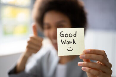 Woman doing thumbs up and holding post-it with Good work :-)